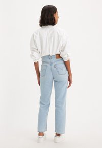 Jeans de cintura alta azul claro com um corte afunilado, um patch de couro na parte de trás e dois bolsos traseiros; combinados com uma camisa branca de corte solto.