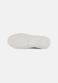 White sneaker sole with textured rubber, circular and linear patterns, featuring a logo inset and pronounced tread for traction.