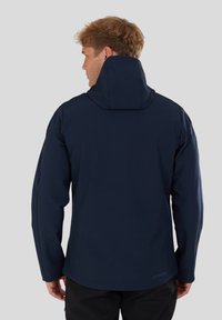 Giacca impermeabile blu navy con cappuccio, tessuto liscio, design aderente e branding discreto vicino all'orlo. Presenta cuciture svelte.