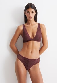 Set di lingerie bordeaux composto da un bralette con scollatura a V profonda e motivo a onde testurizzato, insieme a slip abbinato con pizzo e fianchi con aperture.