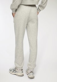 Jasnoszare bawełniane dresy z elastycznym paskiem w talii, kieszeniami po bokach i ściągaczami u dołu. Noszone z jasnoszarymi i czarnymi butami sportowymi.