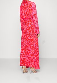 Maxikleid in Rot mit pinkem Tiermuster, langen Ärmeln, tailliertem Schnitt und fließendem Rock. Vervollständigt durch silberne High Heels.