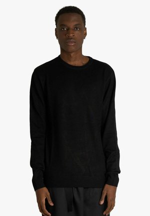 Maglione nero a girocollo in maglia, maniche lunghe, polsini e orlo a coste, tessuto morbido, design semplice, silhouette aderente, indossato con pantaloni scuri.