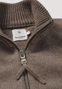 Brauner Strick-Pullover mit Reißverschluss, ausgestattet mit einem gerippten Kragen, einem Metall-Reißverschluss und einem Stoffetikett mit der Marke "hessnatur" und der Größe "M."