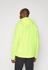Neon-gelbes, leichtes Jacket mit Kapuze. Verfügt über reflektierende Akzente, einen Rückenschlitz und elastische Bündchen. Glattes, wasserabweisendes Material.