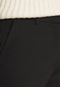 Zwarte broek met een gladde textuur, subtiele stiksel-details en een enkele zichtbare zak, gecombineerd met een crèmekleurige gebreide trui.