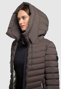 Dunkelbraune Puffjacke mit einer großen, strukturierten Kapuze, Reißverschluss vorne und glänzender silberner Innenauskleidung. Durchgängiges gestepptes Muster.
