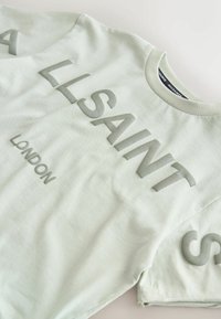 Světlezelené bavlněné tričko s výrazným vystouplým šedým nápisem "ALLSAINTS LONDON" přes přední část. Krátké rukávy, kulatý výstřih.
