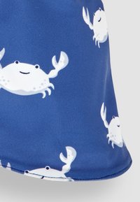 Tessuto blu con un motivo ripetuto di granchi bianchi con facce sorridenti e chelev alzate, texture liscia e bordo arrotondato nella parte inferiore.
