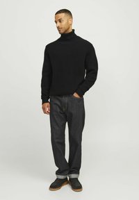 Schwarzer gerippter Rollkragensweater kombiniert mit dunklen Jeans, ausgestattet mit umgeschlagenen Bündchen und schwarzen Schuhen mit brauner Sohle. Minimalistisches Design.