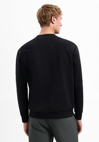 Zwarte sweatshirt met lange mouwen en geribbelde manchetten. Heeft een klassieke ronde hals en een gestructureerde stof, met een relaxte pasvorm.