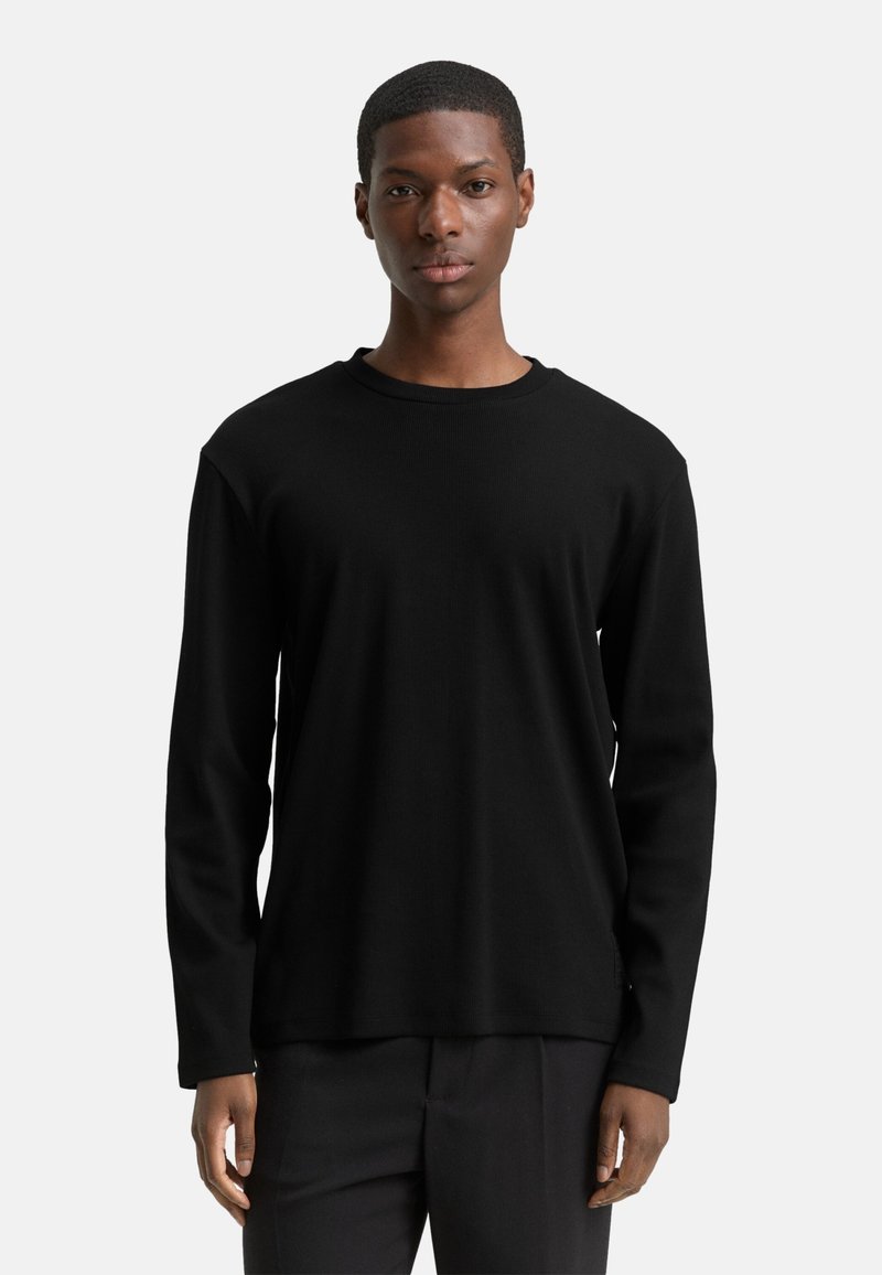 Czarna koszula z długim rękawem wykonana z prążkowanej tkaniny. Posiada okrągły dekolt i luźny fason, zestawiona z czarnymi spodniami. Minimalistyczny design.