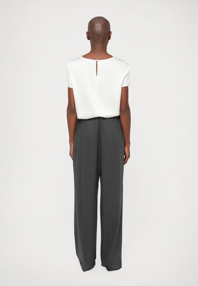 Λευκό μπλούζα κοντομάνικη με λεπτομέρεια κλειδώματος στην πλάτη, συνδυασμένη με ψηλοκάβαλες, φαρδιές σκούρες γκρίζες παν trousers. Λείος ύφασμα με δομημένη σιλουέτα.