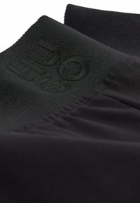 Tissu sportif noir avec un logo en relief. Les caractéristiques incluent une texture lisse, un design extensible et un détail de ourlet froncé.