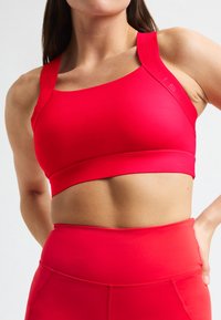Rode sportbeha van gladde stof, met brede banden en een naadloos ontwerp. Gecombineerd met bijpassende hoge taille legging.
