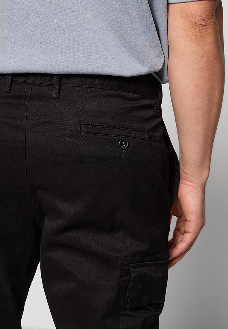 Un pantalon cargo noir en tissu texturé, avec plusieurs poches et une fermeture à bouton. La taille comprend des passants de ceinture pour ajuster la taille.