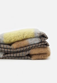 Pile de trois écharpes en laine pliées présentant des motifs à carreaux et unis dans des tons beige, marron, jaune et gris.