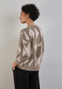 Lehký, oversized svetr v béžové barvě s bílými geometrickými vzory. Měkká textura, kulatý výstřih a tříčtvrteční rukávy.