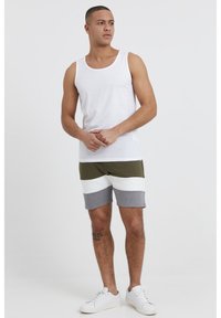 Biała bawełniana koszulka na ramiączkach w połączeniu z zielonymi, białymi i szarymi spodniami w paski. Model ma na sobie białe sneakersy. Prosty, swobodny strój sportowy.