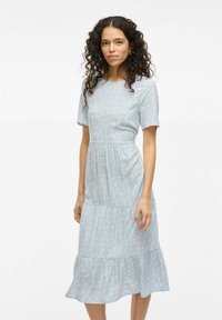 Robe bleu clair avec des manches courtes, un ourlet à volants superposé et un délicat motif floral. Fabriquée en tissu doux et léger.