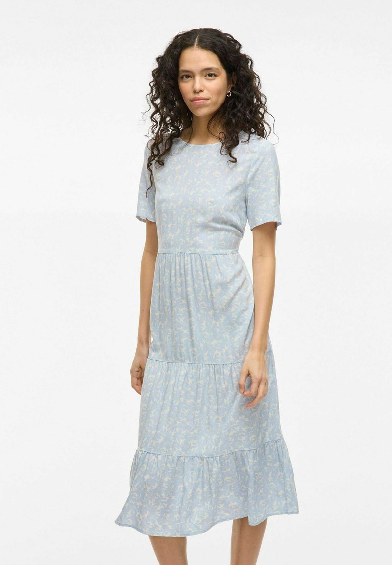 Robe bleu clair avec des manches courtes, un ourlet à volants superposé et un délicat motif floral. Fabriquée en tissu doux et léger.