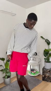 Camisa de manga longa às riscas em branco e preto, combinada com calções vermelhos brilhantes com um pequeno logótipo. Tecido macio e corte descontraído.