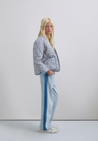 Chaqueta acolchada con un patrón floral azul, combinada con jeans de un azul claro que tienen una franja lateral de un azul oscuro. Zapatillas blancas completan el conjunto.