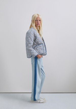 Chaqueta acolchada con un patrón floral azul, combinada con jeans de un azul claro que tienen una franja lateral de un azul oscuro. Zapatillas blancas completan el conjunto.