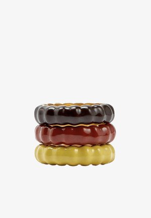 Stos trzech błyszczących, żebrowanych ceramicznych pierścieni w kolorze czarnym, głębokiej czerwieni i musztardowożółtym na białym tle.