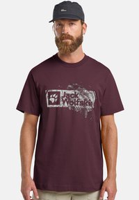 Bordeaux katoenen t-shirt met een versleten witte afbeelding van een pootafdruk en de tekst "Jack Wolfskin". Korte mouwen, ronde hals.