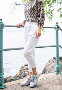 Lehké šedé tenisky se šňůrkami, texturovaná látka, kulatá špička; spárovány s bílými kalhotami s elastickým pasem a hnědým vzorovaným topem s dlouhým rukávem.