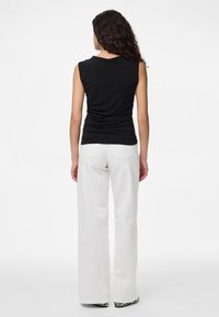 Black sleeveless top with gathered design, paired with high-waisted white wide-leg jeans. Black and white patterned footwear visible.