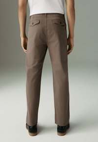 Brown straight-leg pants with a smooth texture, two rear pockets, and belt loops, paired with black shoes, viewed from the back.