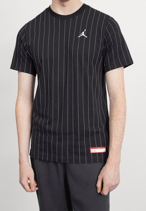 Camiseta negra de manga corta con finas rayas verticales blancas, logo Jumpman blanco en el pecho y un pequeño parche rojo y blanco cerca del dobladillo.