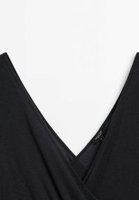 Czarna bluzka o kroju kopertowym z głębokim dekoltem w kształcie V, wykonana z gładkiego materiału. Tekstura jest miękka, z minimalistycznymi szwami i widoczną metką wewnątrz.