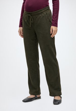 Personne portant un pantalon en velours côtelé vert olive à cordon, un haut bordeaux à manches longues et des chaussures plates noires à brides arrière sur fond blanc.