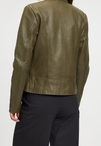 Olivengrön läderjacka med skräddarsydd passform, som har en slät yta, distinkta sömmar och en minimalistisk design. Bakåtvyn visas.