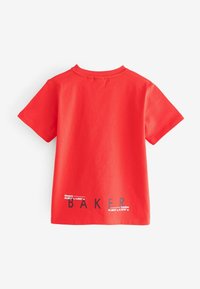 Camiseta de algodón roja de manga corta con texto negro y coordenadas cerca del dobladillo, con "BAKER" destacado.