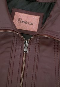 Burgunderfarbene Lederjacke mit einem silbernen Reißverschluss, vertikalen Nähten und einem rosa strukturierten Etikett mit dem Markennamen "Caminari."