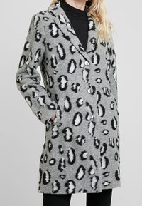 Grå ullblandad kappa med svart- och vitprickig leopardmönster, snedkrage, sidofickor och knappstängning. Mjuk textur och knälängd.