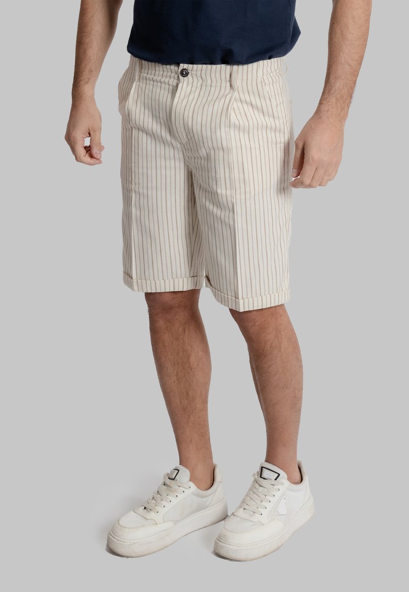 Shorts a righe chiare in un tessuto morbido, con chiusura a bottone, tasche laterali e orlo arrotolato, abbinati a sneakers bianche.