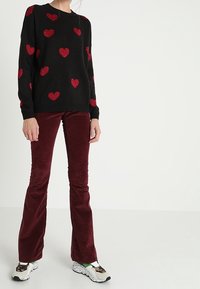 Musta neulepaita punaisilla sydänkuvioilla, yhdistetty viininpunaisiin samettikorvakkeisiin liehuhousuihin. Kengissä on pilkullinen pohja ja vihreitä yksityiskohtia.