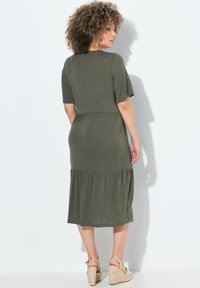 Vestido verde oliva de longitud a la rodilla con mangas cortas, cintura fruncida y falda en capas. Tejido ligero con una textura suave.