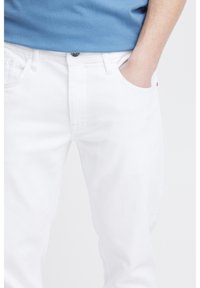 Jeans de mezclilla blanca con corte recto, que cuentan con un cierre de botón único, cinco bolsillos y acentos de costura mínimos.
