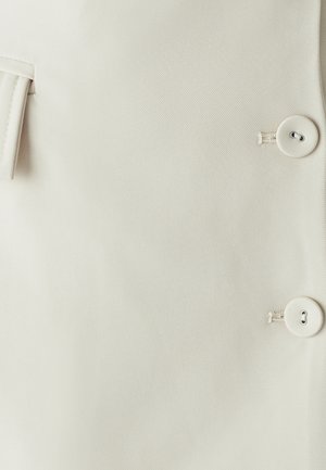 Bežinė medžiaga su tekstūruota paviršiumi, turinti dvi dideles mygtukus ir šoninę kišenę. Švarus, paprastas dizainas su minimaliais detalėmis.