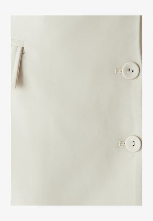 Bežinė medžiaga su tekstūruota paviršiumi, turinti dvi dideles mygtukus ir šoninę kišenę. Švarus, paprastas dizainas su minimaliais detalėmis.