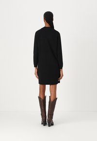 Melna sporta kleita ar garām piedurknēm, brīva piegriezuma un apaļu kakla izgriezumu, apvienota ar brūnām ceļgala augstām rietumu stila zābakiem.