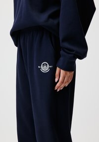 Navyblaue Jogginghosen aus weichem Stoff, mit einem elastischen Bund und einem weißen gestickten Logo mit "Est. 2017" auf der linken Seite.