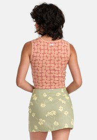 Fitted, sleeveless top in peach with floral pattern; paired with a green skirt featuring yellow flower prints.