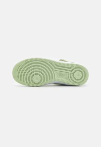 White sneaker sole with a textured, mint green rubber base featuring circular patterns and a prominent Nike logo.